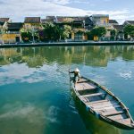 Peaceful scene of a traditional boat on the serene river in Hội An, Vietnam, showcasing historic architecture.