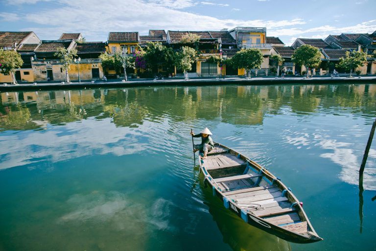 Peaceful scene of a traditional boat on the serene river in Hội An, Vietnam, showcasing historic architecture.